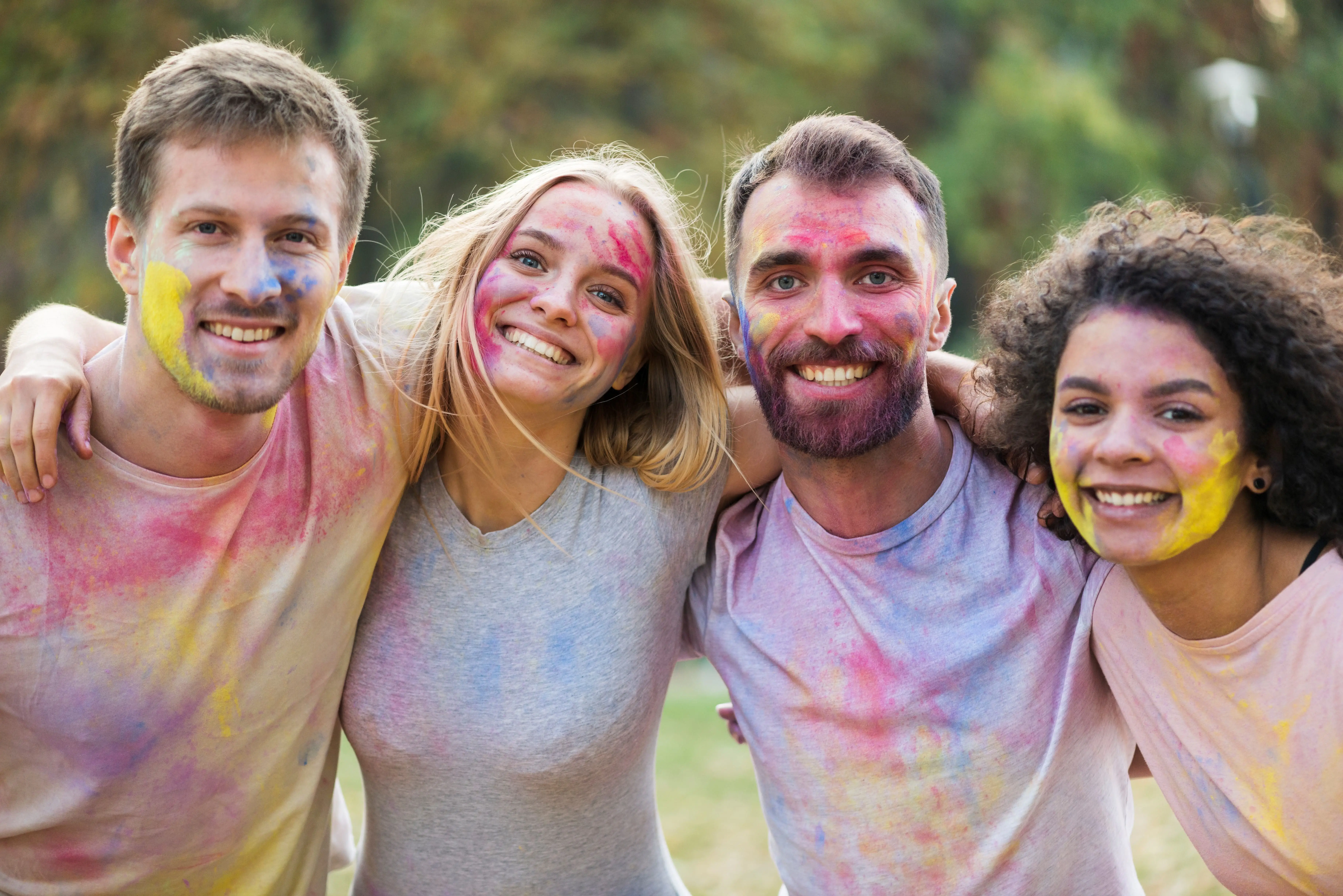 Quatro jovens sorridentes abraçados com as roupas e corpos coloridos