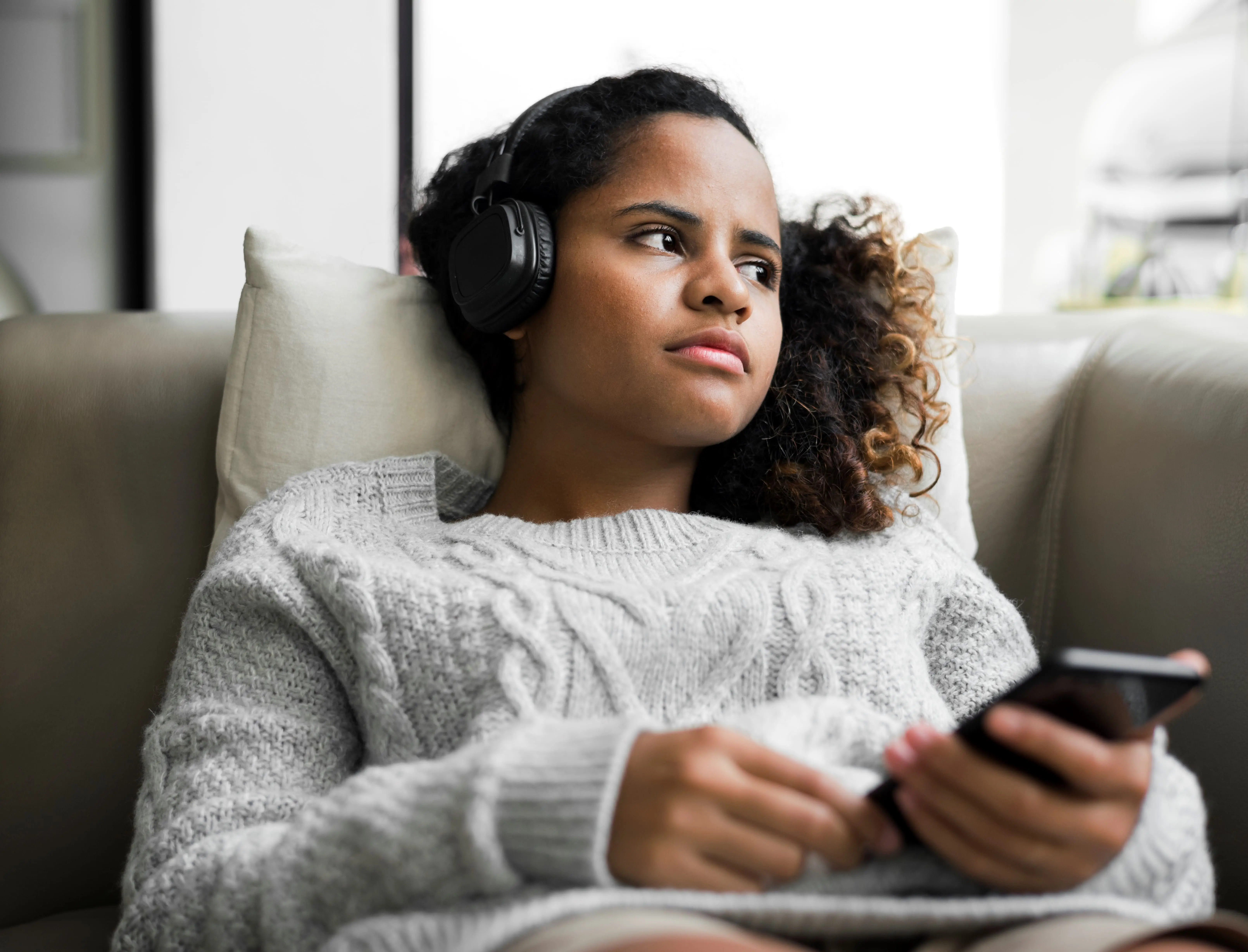 Mulher sentada com o celular na mão, usando fone de ouvido e com olhar distante